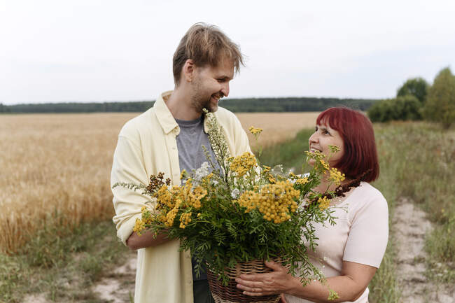 Uomo sorridente che tiene un cesto di fiori di tanaceto con madre — Foto stock