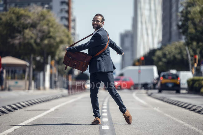 Happy businessman with crossbody bag spinning on road — Stock Photo