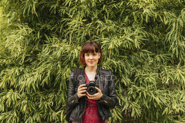 Fotógrafo feminino com franja segurando câmera na frente de plantas — Fotografia de Stock