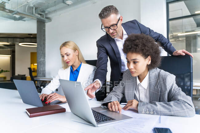 Male business professional explaining female colleague over laptop at desk — Stock Photo