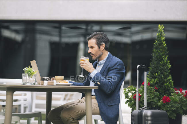 Homme d'affaires mature buvant du jus tout en travaillant sur un ordinateur portable à l'hôtel — Photo de stock