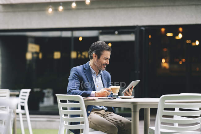 Усміхаючись бізнесмен користується цифровим планшетом, коли пив каву в готелі. — стокове фото