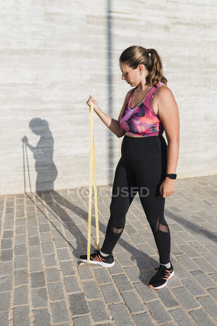 Young female athlete with resistance band practicing during sunny day — Stock Photo
