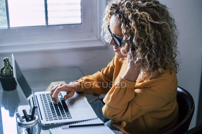 Femme aux cheveux bouclés freelance travaillant sur ordinateur portable à la maison — Photo de stock