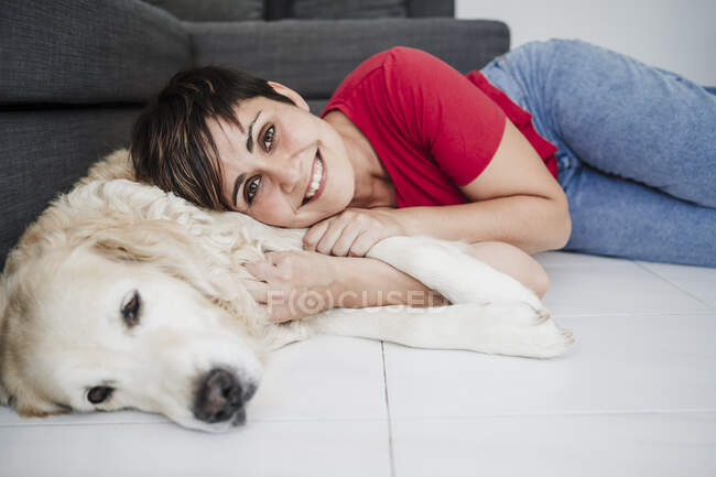Усміхнена жінка середнього віку лежить удома з собакою. — стокове фото