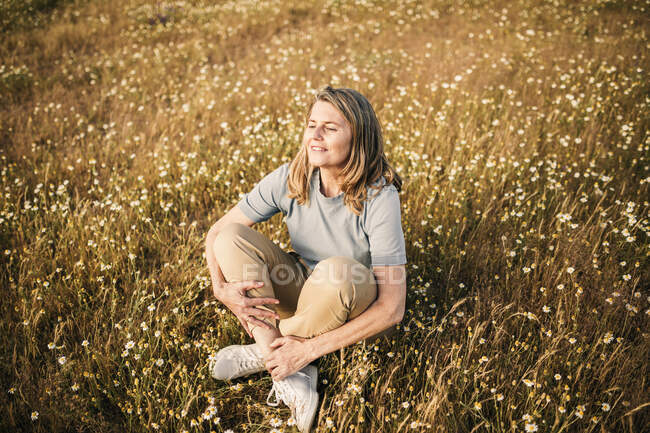 Sorrindo mulher madura com cabelo loiro sentado no campo — Fotografia de Stock