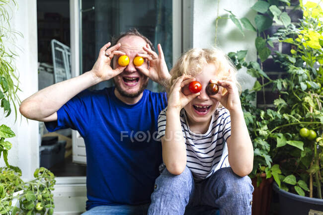 Heureux père et fils couvrant les yeux de tomates tout en étant assis sur le balcon — Photo de stock