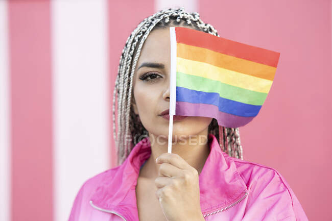 Jovem mulher cobrindo os olhos com bandeira do arco-íris por parede — Fotografia de Stock
