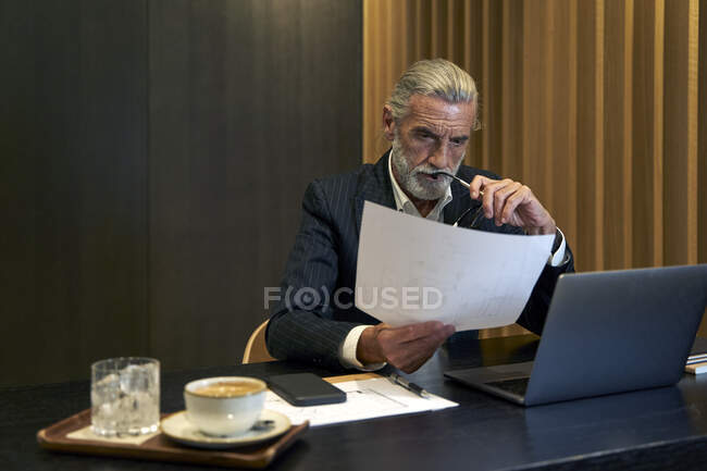 Homme d'affaires mature lisant un document assis au bureau — Photo de stock