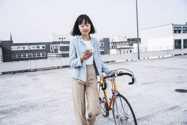 Ragazza adolescente con bicicletta utilizzando il telefono cellulare sul tetto — Foto stock