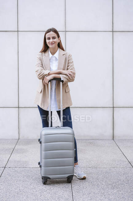 Young businesswoman with wheeled luggage standing on footpath — Stock Photo