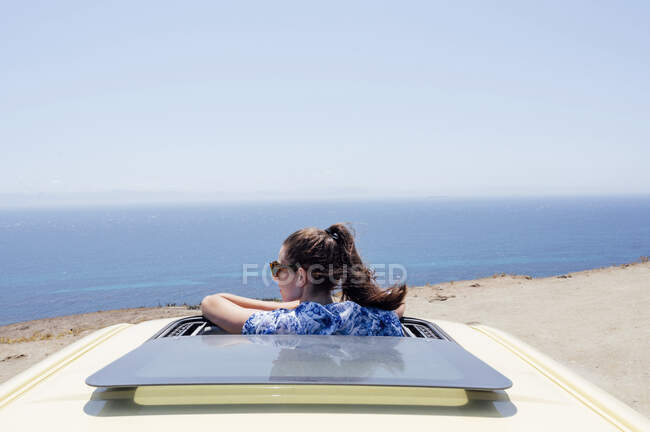 Mujer adulta mediana con gafas de sol inclinadas a través del techo solar de la furgoneta durante el verano - foto de stock