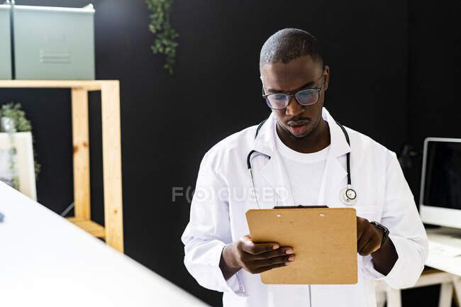 Hombre doctor leyendo portapapeles en clínica médica - foto de stock