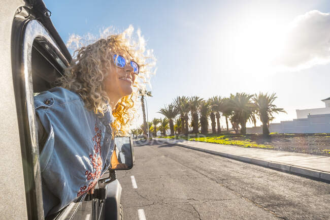 Smiling woman leaning from car window during sunny day — Stock Photo