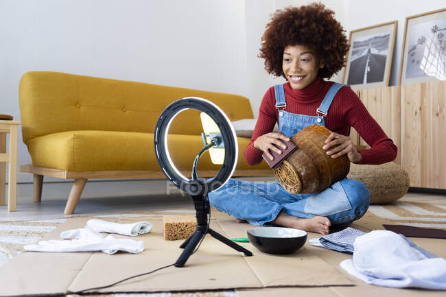 Female influencer polishing wicker basket while vlogging through smart phone at home — Stock Photo