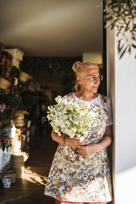 Thoughtful female florist with flowers standing at shop entrance — Stock Photo