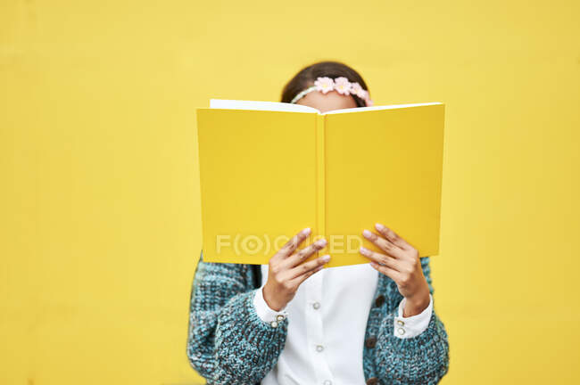 Giovane donna che legge libro giallo da parete — Foto stock