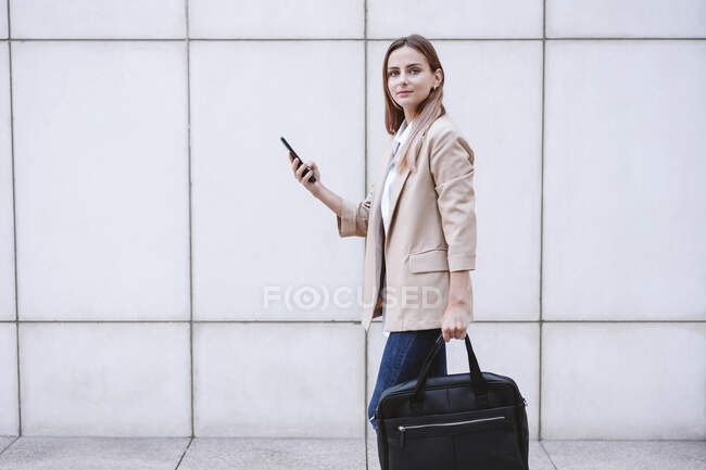Giovane donna d'affari con valigetta e smartphone che cammina sul sentiero — Foto stock