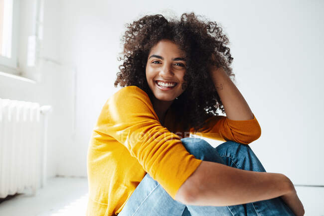 Mulher sorridente com a mão no cabelo sentado no chão em casa — Fotografia de Stock
