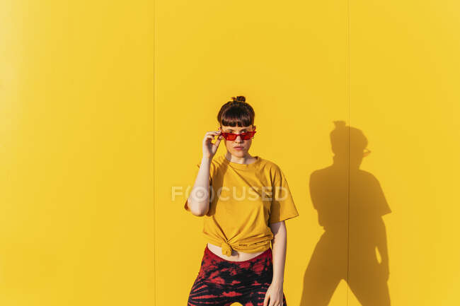 Femme adulte moyenne portant des lunettes de soleil devant un mur jaune pendant la journée ensoleillée — Photo de stock