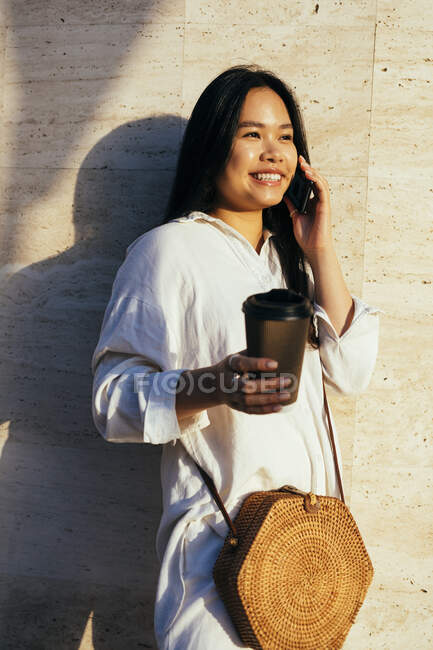 Mulher feliz usando saco crossbody falando no telefone celular por parede — Fotografia de Stock