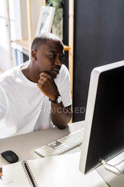 Männlicher Freiberufler sitzt mit der Hand am Kinn und blickt auf den Desktop-Computer im Studio — Stockfoto