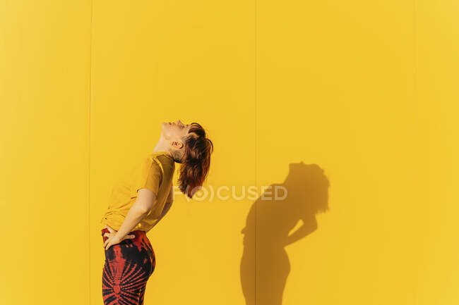 Femme avec la main sur la hanche debout par le mur pendant la journée ensoleillée — Photo de stock