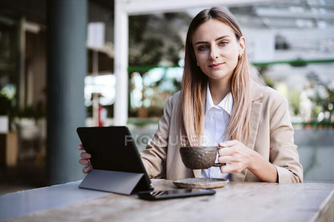 Жіночий бізнесмен з цифровим планшетом і чашечкою кави сидить за столом. — стокове фото