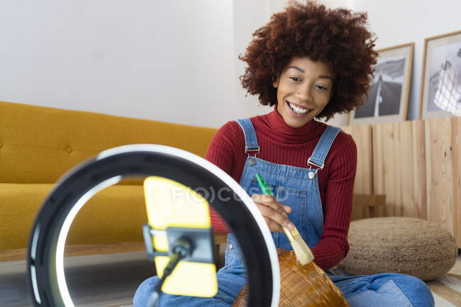 Weibliche Influencerin malt Korbflechter, während sie zu Hause mit dem Handy surft — Stockfoto