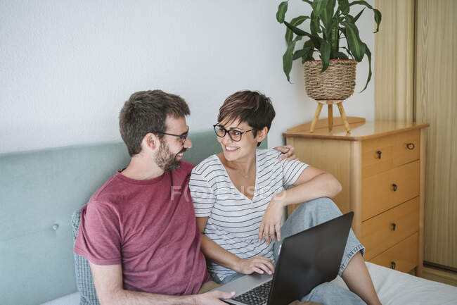 Lächelndes erwachsenes Paar mit Laptop zu Hause im Bett — Stockfoto