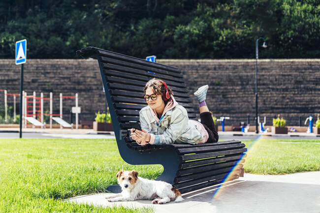 Donna che utilizza il telefono cellulare mentre sdraiato su panchina da cane al parco — Foto stock