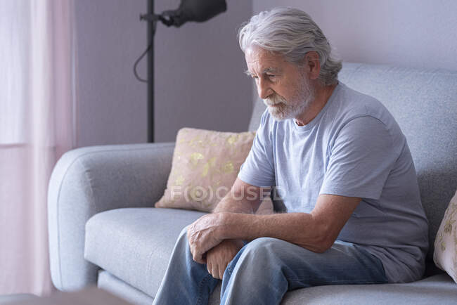 Hombre mayor solitario sentado en el sofá en casa - foto de stock