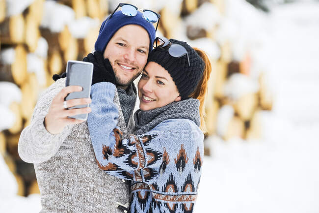 Couple en tricot chapeaux prendre selfie par téléphone intelligent pendant l'hiver — Photo de stock
