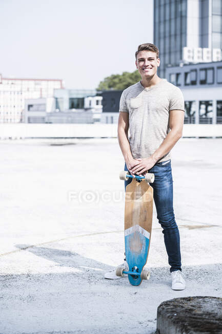 Jeune homme souriant avec planche à roulettes debout sur le toit — Photo de stock