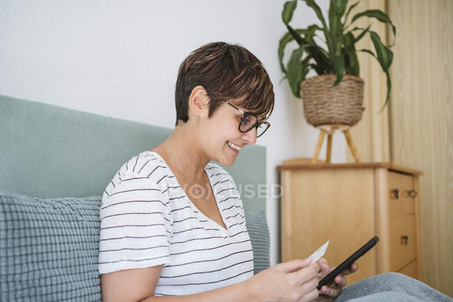 Frau benutzt Smartphone, während sie Kreditkarte zu Hause hält — Stockfoto