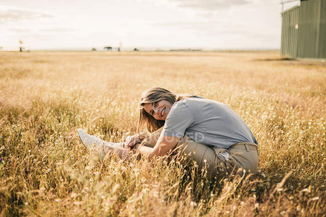 Жінка посміхається, обіймаючи коліна на сільськогосподарському полі. — стокове фото