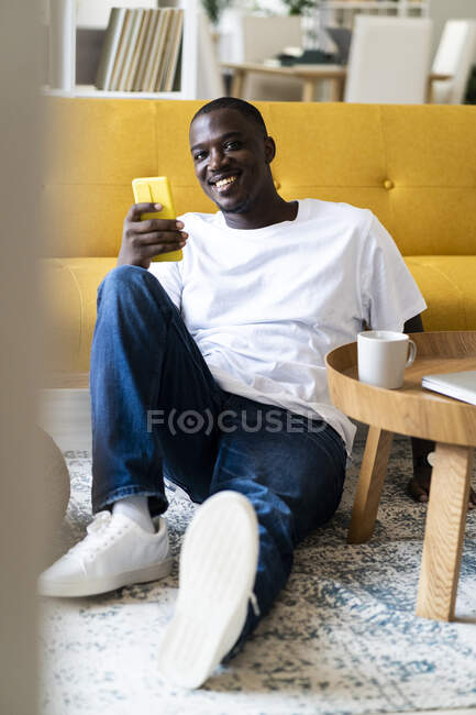 Uomo con smart phone seduto su tappeto a casa — Foto stock