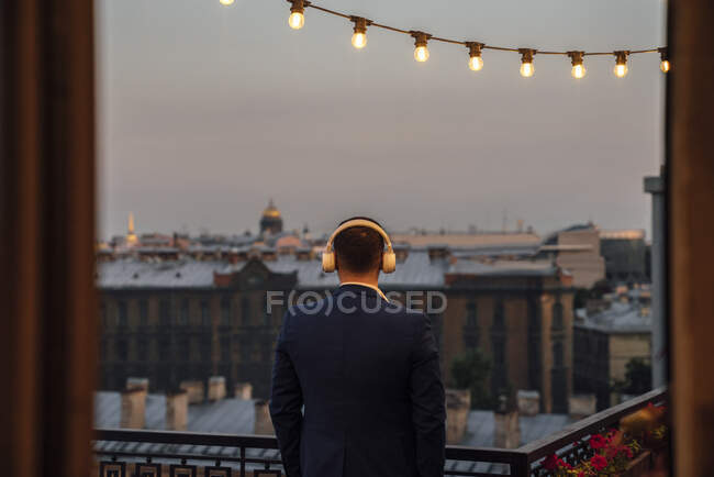 Мужчина, занимающийся бизнесом, смотрит на здания, слушая музыку на закате — стоковое фото