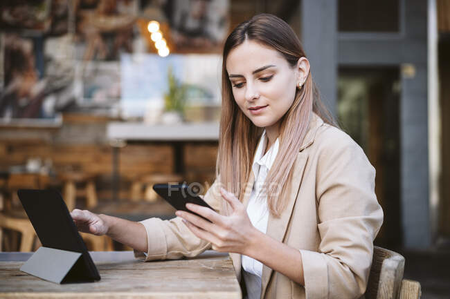 Деловая женщина с цифровым планшетом с помощью смартфона на террасе кафе — стоковое фото