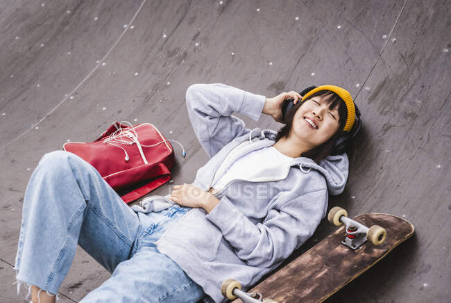 Ragazza adolescente che ascolta musica attraverso le cuffie wireless allo skateboard park — Foto stock