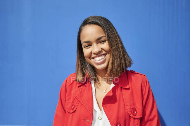 Mujer joven sonriente frente a la pared azul - foto de stock