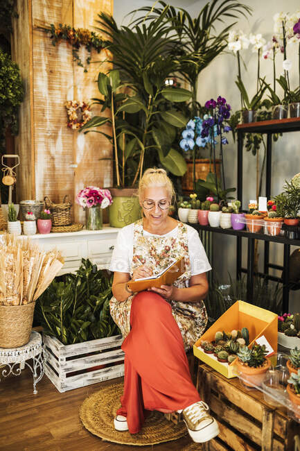 Fiorista donna che scrive nel libro seduta nel negozio di fiori — Foto stock