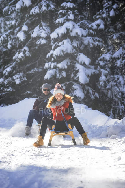 Улыбающаяся женщина катается на санках с мужчиной по снегу зимой — стоковое фото