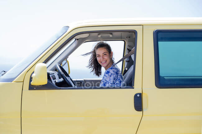 Happy mid adult woman sitting in yellow camper van during sunny day — Stock Photo