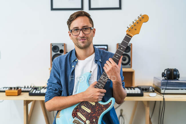 Guitarrista masculino usando óculos segurando guitarra em casa — Fotografia de Stock