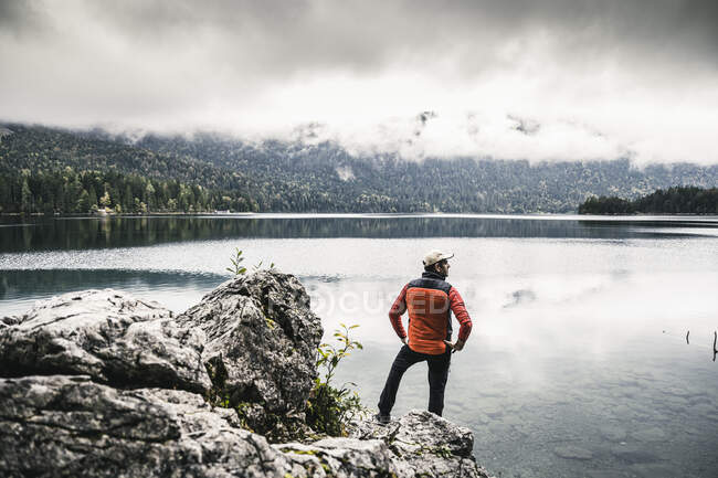 Homme avec les mains sur la hanche debout sur le rocher au bord du lac — Photo de stock