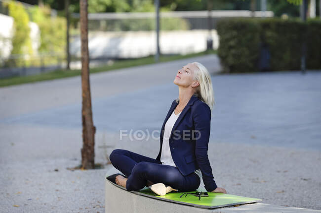 Businesswoman relaxing while sitting cross-legged on retaining wall — Stock Photo