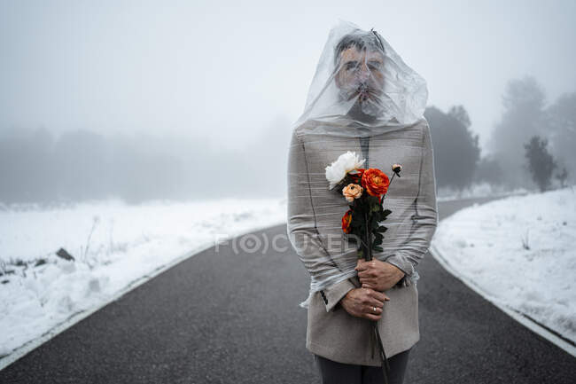 Homem maduro envolto em plástico segurando cacho de flores na estrada — Fotografia de Stock