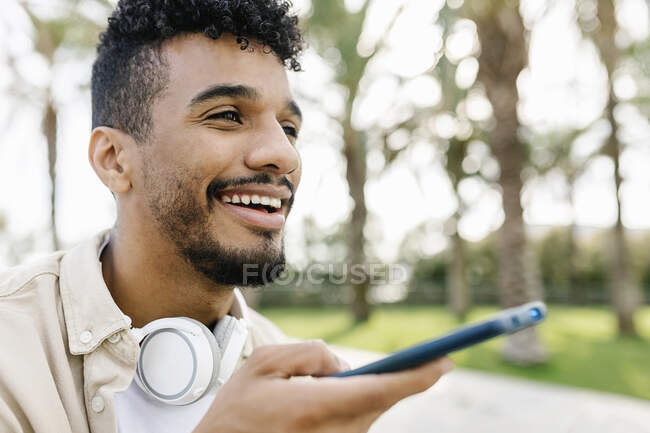 Uomo sorridente con cuffie wireless che parla tramite altoparlante su smartphone — Foto stock