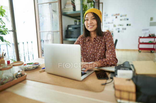 Female professional wearing knit hat sitting with laptop at workplace — Stock Photo
